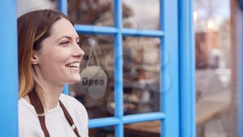 Smiling Female Small Business Owner Standing In Shop Doorway On Local High Street