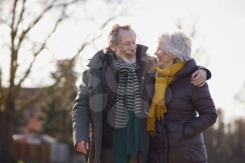 Loving Senior Couple Enjoying Autumn Or Winter Walk Through Park Together