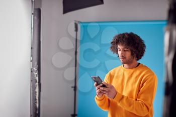 Studio Portrait Of Young Man Looking At Mobile Phone Against Blue Background