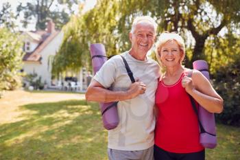 Portrait Of Senior Couple At Home In Garden Wearing Fitness Clothing Ready For Outdoor Yoga Session
