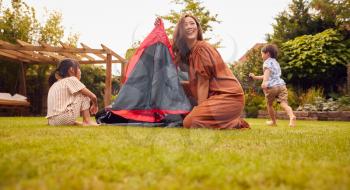 Asian Mother With Children In Garden At Home Putting Up Tent For Camping Trip Together