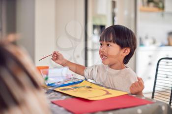 Young Asian Boy Painting Picture And Having Fun Doing Craft On Table At Home