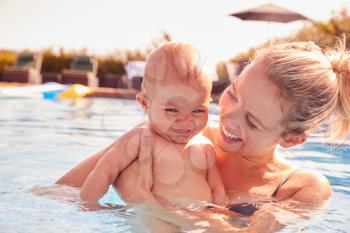 Mother With Baby Daughter Having Fun On Summer Vacation Splashing In Outdoor Swimming Pool