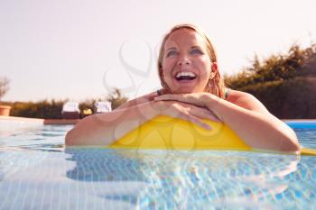 Woman Having Fun With Inflatable On Summer Vacation In Outdoor Swimming Pool
