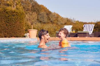 Father And Son In Outdoor Pool On Summer Vacation Teaching Son To Swim With Inflatable Armbands