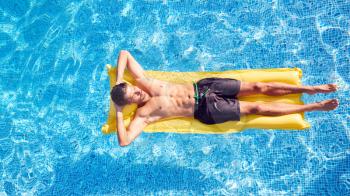 Overhead Shot Of Man In Swim Shorts Floating On Air Bed On Summer Vacation In Outdoor Swimming Pool