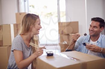Couple Celebrating With Takeaway Sushi Meal Sitting On Floor Of New Home On Moving Day