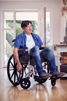 Mature Asian Man In Wheelchair Pushing Himself Along Hallway At Home