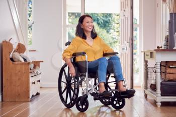 Mature Asian Woman In Wheelchair Pushing Herself Along Hallway At Home