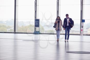 Business Couple At Railway Station Wearing PPE Face Masks Holding Hands Walking Across Concourse