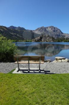 Cosy bench on the shore of Seagull Lake. A bright sunny day, the mountain is reflected in the smooth water of the lake