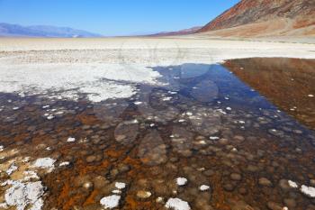 The famous section of Death Valley - Bad Water. Very salty puddle on the covered crystal salt stones. Blinding midday sun
