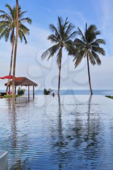 The magnificent swimming pool built on the beach of Koh Samui.  The dark blue ocean distance and pool are divided by three picturesque palm trees and beach pavilions