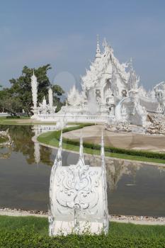 Fantastic beauty White Temple in South East Asia. Perfectly well decorated facade is reflected in a pond with live small fishes
