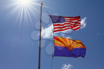 Flags of the United States and the Navajo Reservation are flying against the shining sun and clouds