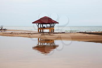 Sandy beach on Koh Samui. The beach wooden arbor is picturesquely reflected in water
