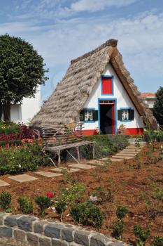 Classical small house  on Madiera. A bright red door, a straw triangular roof, a small front garden and an accurate stone path
