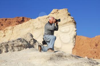 Tourist photographing the canyon on the coast of the Dead Sea. For convenience, he dropped to one knee