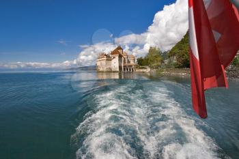 The well-known palace museum  ?hillon on coast of lake Leman in Switzerland, a foamy trace on water and a flag of Switzerland