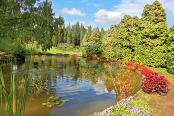 Charming park Sigurta in northern Italy. Picturesque bushes with red flowers at a round pond