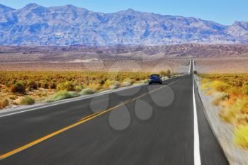 The blue car was going at high speed, crossing Death Valley in the USA. The low dry bushes and mountains