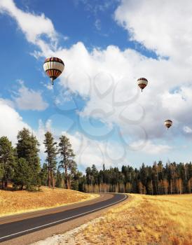 Huge balloons with a passenger basket fly over charming rural road
