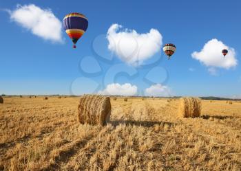 Three colorful balloons flying slowly over the field after harvest. Stacks of harvested wheat beautifully  stand in rows