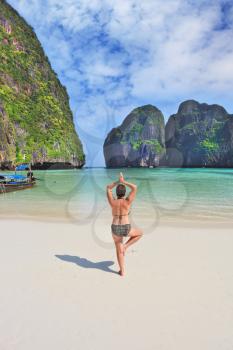The tightened elderly woman goes in for hatha-yoga on a beach. Maya Bay Island in the Andaman Sea, Thailand