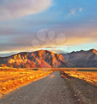 Argentina Patagonia. Perito Moreno's huge and magnificent national park. The gravel road between boundless Pampas. The sunset sun shines mountains and the steppe with red light