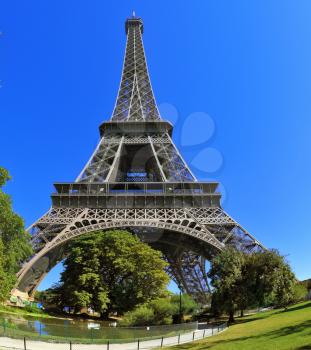 The most famous in the world - the Eiffel Tower in the background of bright blue sky. At the foot of the tower - a park and a large pond. The picture was taken by lens Fisheye