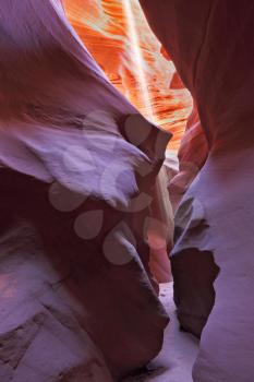 A thin ray of sunlight illuminates the sandy bottom of the canyon. Noon in a red-orange Antelope Canyon. 
