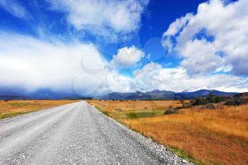 A dirt road in the endless pampas. Strong wind drives the clouds. On the horizon, the mountains visible in the haze