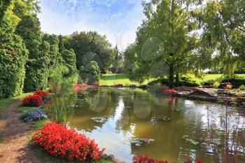 Picturesque bushes with red flowers at a silent pond. Charming park Sigurta in northern Italy. 