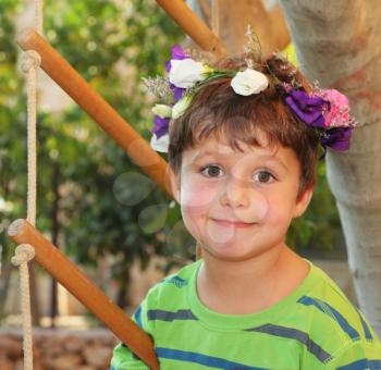 Cheerful birthday beautiful boy in the park. The boy wore a wreath of flowers