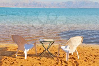 Sunny beach on the Dead Sea. A wonderful warm day in December. Beach chairs and a table waiting for tourists