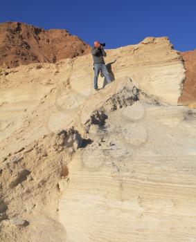 The gray-haired man photographs in a canyon at coast of the Dead Sea. On a shoulder at it a bag of the professional photographer.