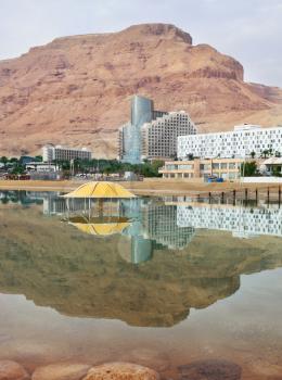 Winter in the Dead Sea. The comfortable high-rise hotel and ancient mountains are reflected in the sea smooth water
