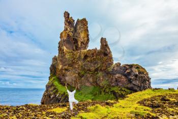 Woman in white performs asana Tree. The ancient rocks covered with a green and yellow moss. Iceland. Northern coast of Atlantic