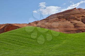 Bright green field for a golf among hills from red sandstone