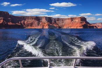 Walk on the tourist boat. Foam boat trail crosses the emerald waters. Red sandstone hills surround the lake. Lake Powell on the Colorado River