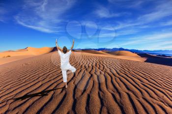 Yoga in the desert. Orange sand dunes in Death Valley, California. A middle-aged woman in a white performs asana Tree on one leg
