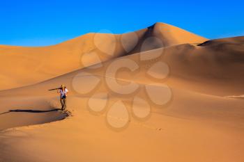 Woman - photographer in a striped T-shirt is among the sand dunes. Sunrise in the orange sands of the desert Mesquite Flat, USA