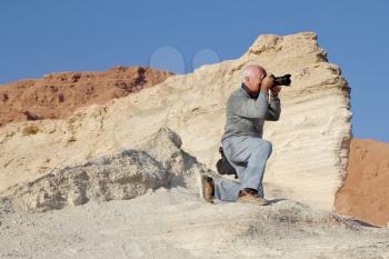 Tourist photographing the canyon on the coast of the Dead Sea. For convenience, he dropped to one knee