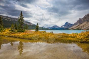 Banff National Park. The smooth water reflects the cloudy sky. Snow-capped mountains and glaciers surroundings Bow Lake