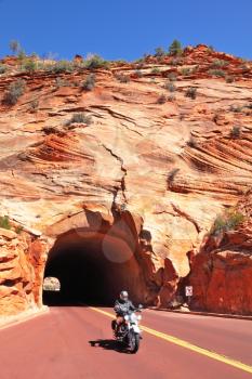 Zion National Park, USA. Motorcyclist leaves the tunnel in the sandstone hill