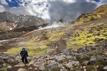 Rhyolite mountains smoldering underground heat. In the hollows lie unmelted snow patches from last year. Mature woman tourist wearing warm up the trail. Iceland in July