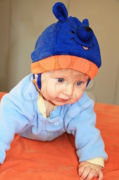 The charming four-months boy with blue eyes in a blue hat with ears tries to creep