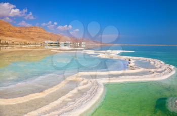 Israeli coast of the Dead Sea. The path from salt picturesquely curls in salty water. Hotels are reflected in smooth water ashore