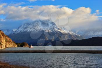 Gray lake and snow-capped mountains. By the banks of the red tourist ship sails. Summer sunset illuminates the lake. National Park Torres del Paine, Chile