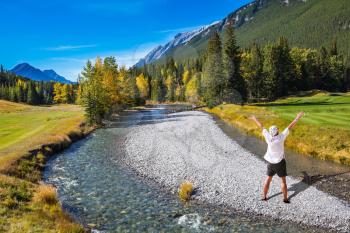 Zonked tourist in white shirt and bandana stands on a rocky shoal creek. Autumn day in the Canadian Rockies, Banff Park